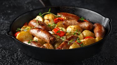 Potato sausage being cooked in a pan with potato, red pepper and onion in cast iron vintage pan.