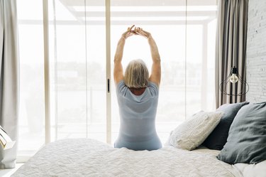 Rear view of elderly woman stretching in bedroom, experience mobility loss