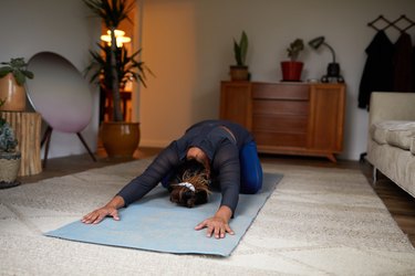 Person doing child's pose on yoga mat in bedroom as part of a strengthening and relaxing workout before bed.