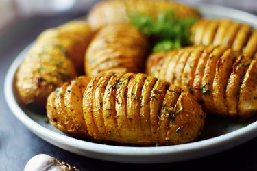 Hasselback potatoes. Baked accordion potatoes. Delicious vegetables. Food in a gray clay plate, close-up.