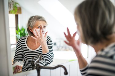 Older woman looking in the mirror, applying a lemon juice and baking soda mask