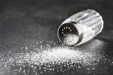 a glass salt shaker spilling on a dark stone table