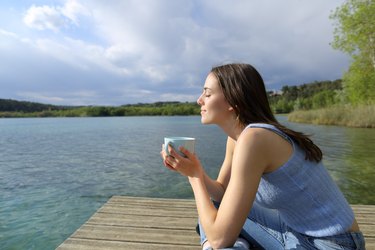 a young adult relaxes drinking a mug of coffee on a pier on a lake