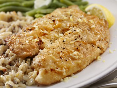 Oven-baked tilapia fish with rice and green beans with lemon on a white plate.