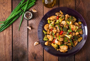 Stir-fry with chicken, mushrooms, broccoli and peppers on wooden table