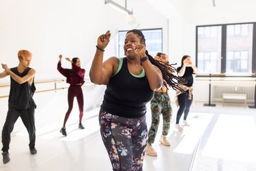 beginners doing basic zumba moves in a class in a white studio