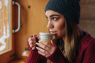 戴着帽子和毛衣的女人喝着一杯绿茶