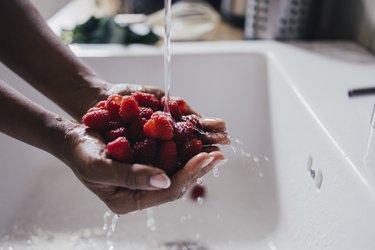 A close up of a person's hands holding raspberries under running water for a fruitarian diet