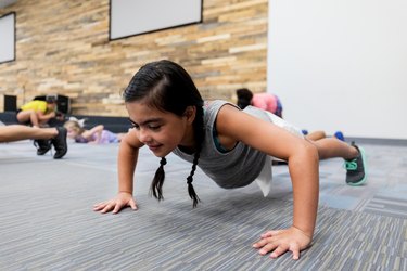 Child with pigtails doing a push-up in a gym