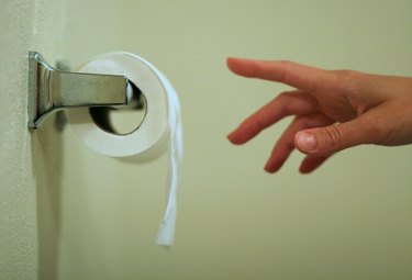 A hand of a person reaching for toilet paper while pooping undigested food