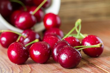 Cherries on wooden table with water drops in the ceramic cup. Closeup. Selective focus