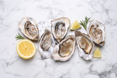 Zinc-rich raw oysters with lemon and rosemary on white marble table.