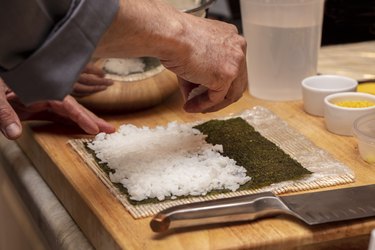 Chef preparing ingredients and packing sushi rice onto seaweed for sushi