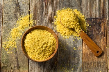 overhead photo of wooden bowl and spoon of raw yellow nutritional yeast on wooden table