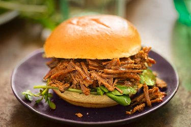 a barbecue beef brisket with barbecue sauce and watercress leaves on a sweet bun on a black plate