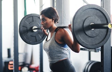 Person in gray tank top and black leggings working out with a barbell