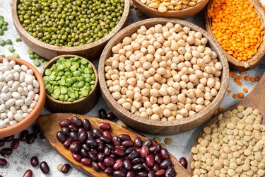 Different legumes. Mung beans, red and white beans, lentils, peas and chickpeas in wooden bowls on the light grey kitchen table. Beans closeup. Vegetarian food