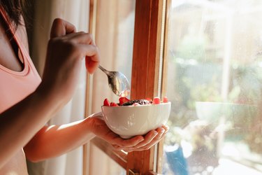 woman eating breakfast bowl of fruit yogurt seeds and chocolate