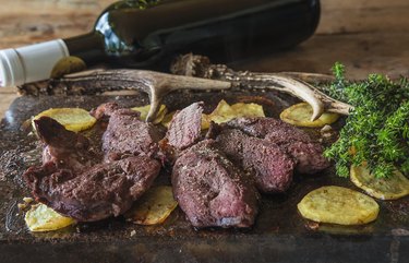 Savory food: venison steaks and fried potatoes on a wooden board with a bottle of wine behind