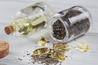 Gelatin capsules with algae omega oil and seaweed on a white wooden background.