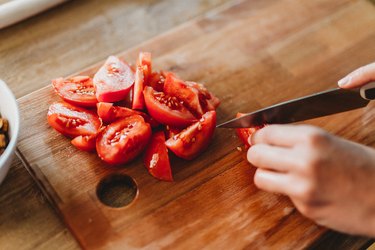 close view of a person cutting up tomatoes on a wooden cutting board