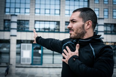 close up of an adult with a short beard and haircut doing an arm stretch because after a bicep workout