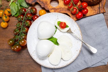 Cheese collection, eating of white soft Italian cheese mozzarella, served with red cherry tomatoes, fresh basil leaves