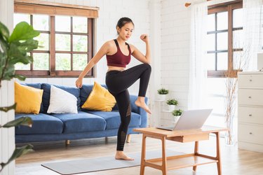 Asian woman following a low-impact cardio workout on her laptop in her living room