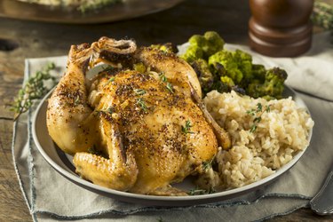 Baked Cornish hens garnished with herbs and rice and veggies on side
