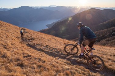 cyclists ride mountain bikes down grassy mountain ridge at sunrise