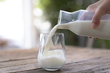 milk, a food high in taurine,  is poured into a ceramic jug into a glass on a natural background.