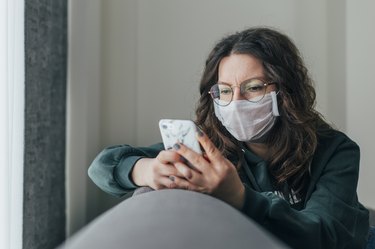 A woman with COVID-19 is wearing a mask and texting in isolation at home