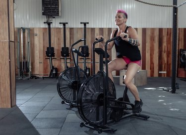 Woman exercising on air bike to get fan bike benefits. Cycling fitness training.  Athletic female using air bike cardio workout. Cross functional training.