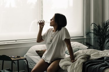 Mature woman sitting on bed in the morning drinking water