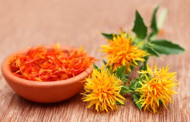 three safflower flowers and a bowl of petals on wooden background