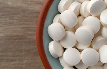 an overhead photo of white DHEA supplements in a small bowl on a wooden table