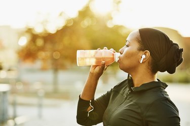 Wwoman drinking sports drink after working out in park on fall afternoon