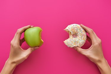 Hands holding an apple and a donut to show the concept of good vs bad food