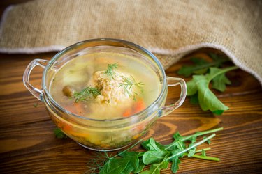 Glass bowl filled with chicken and vegetable soup with arugula on the side