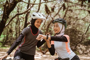 Two happy friends wearing hijabs while riding bikes at the park in zone 2 training