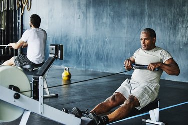 Person in white T-shirt and shorts working out on rowing machine in gym as an example of high-intensity, low-impact exercise