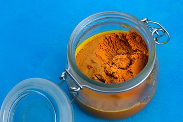 Turmeric paste in a glass jar on a blue background as a natural fat lip remedy