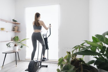 woman wearing gray tank and leggings and working out on the elliptical at home