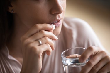 Close up young woman taking pill, holding water glass