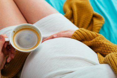Pregnant person drinking a cup of caffeinated coffee