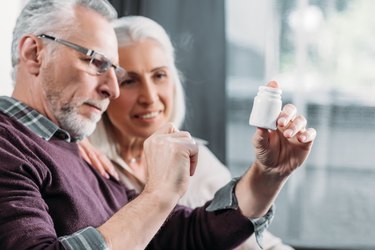 senior man and woman looking at pill bottle in hand