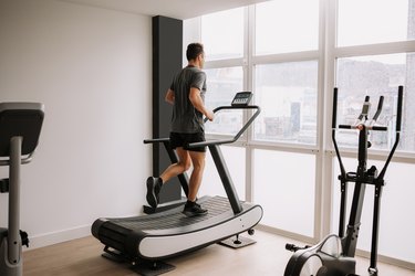 Caucasian adult man running on a treadmill in the gym next to a large window