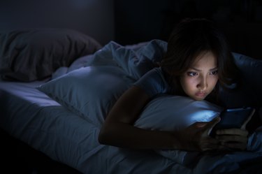 Young woman using a smartphone in her bed at night