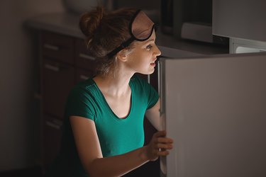 Beautiful young woman looking into fridge at night