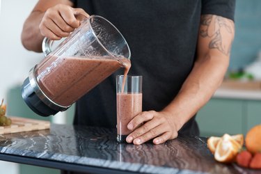 Cropped shot of a person assigned male at birth pouring a pink smoothie from the blender into a glass as part of a liquid diet food list